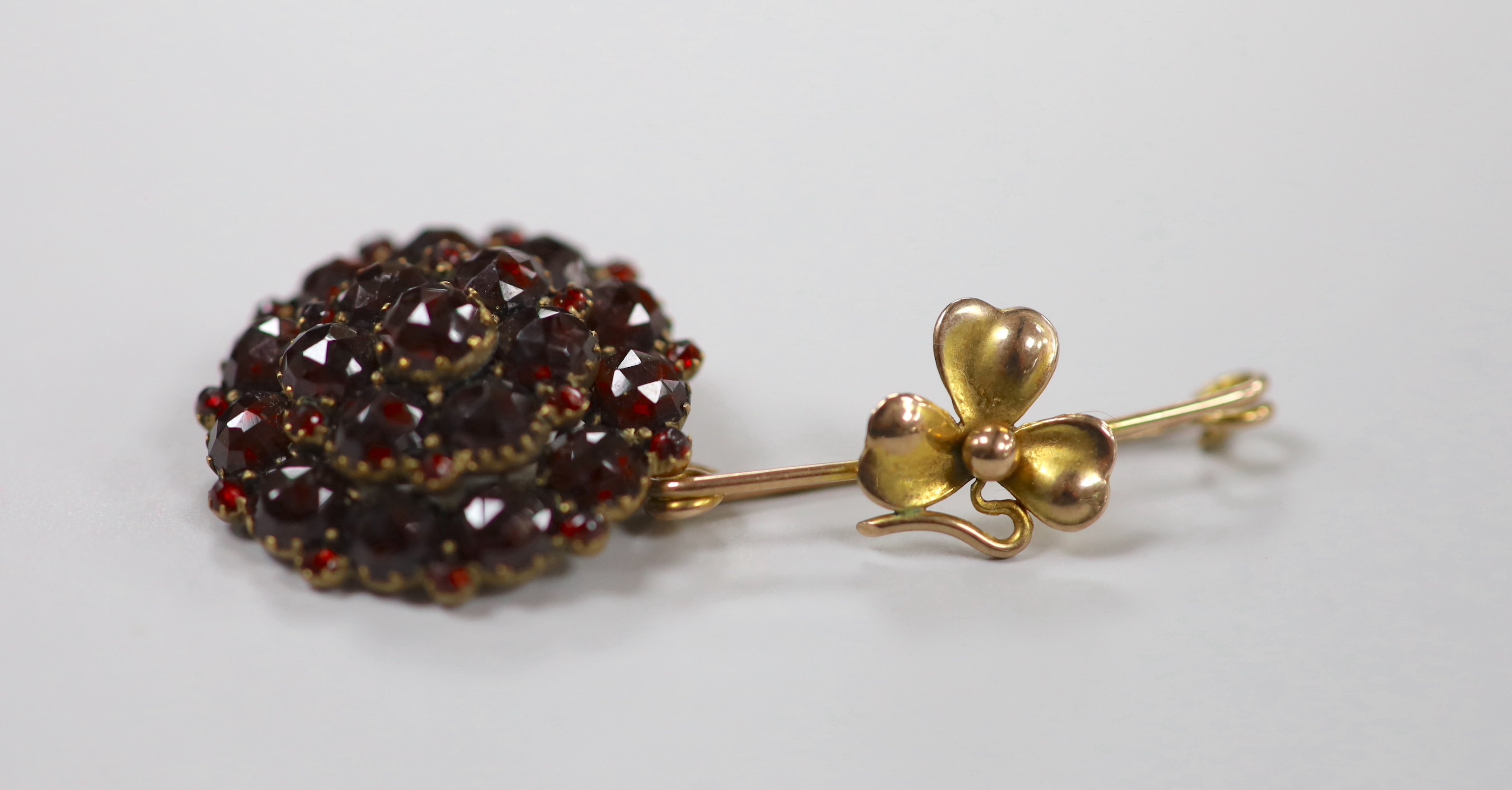 A yellow metal 'shamrock' bar brooch, 36mm, 1.6 grams and a late Victorian gilt white metal and garnet cluster set pendant brooch.